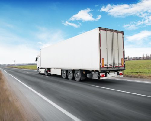 A big white truck and a trailer with space for text on the countryside road in motion against a blue sky with clouds